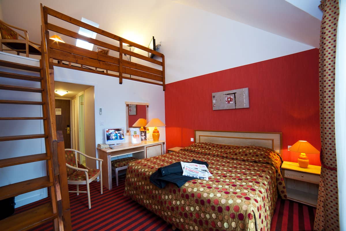 A hotel room with a bunk bed, a desk with a chair, a computer, and a bed with a polka dot bedspread.
