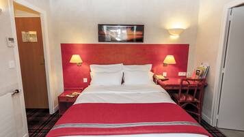 A hotel room with a large bed, two bedside tables, a desk with a chair, a painting on the wall, and a door with a thermostat.
