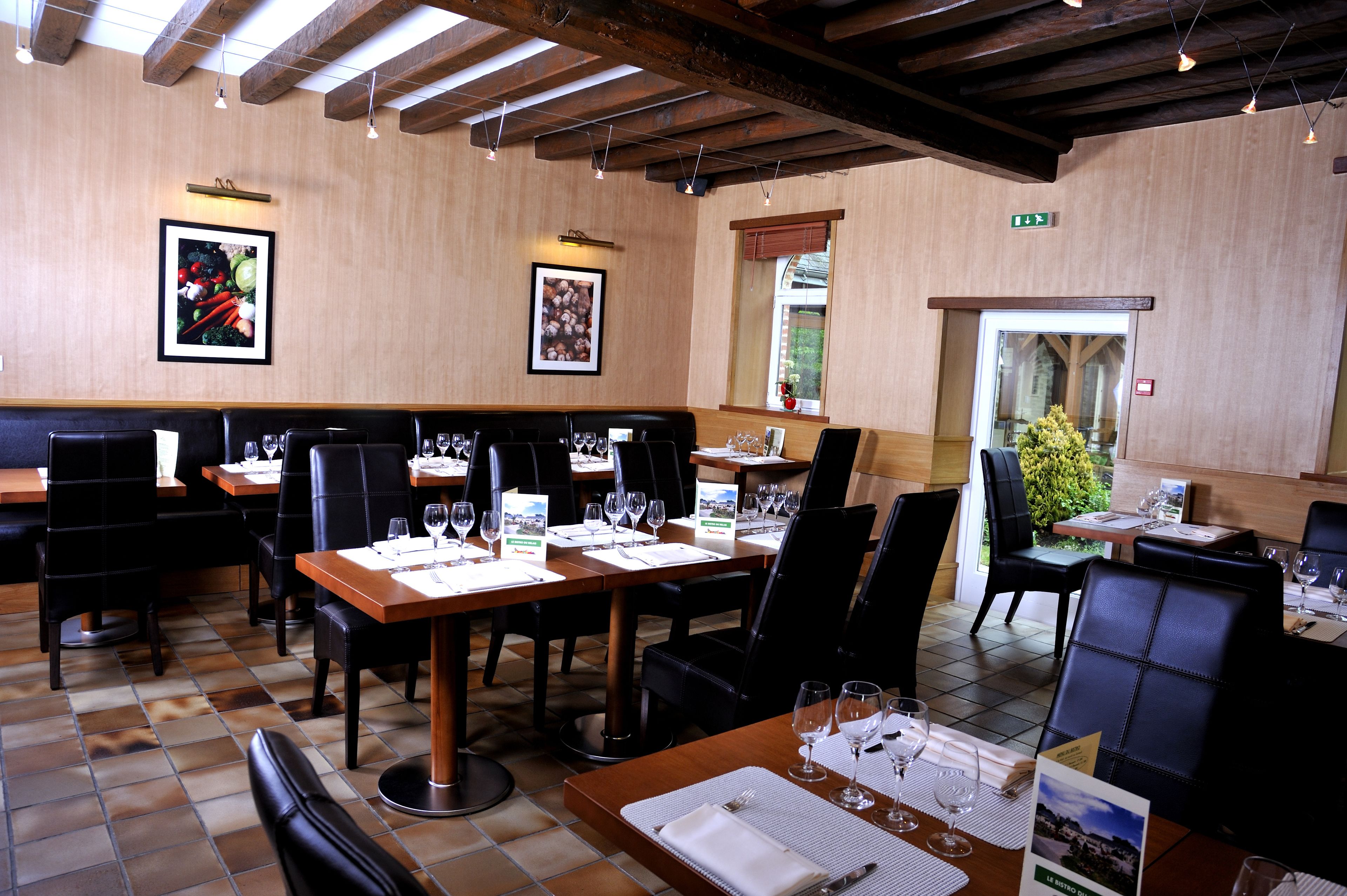 Un restaurant aux murs en bois, aux chaises en cuir noir et aux tables dressées pour le repas.