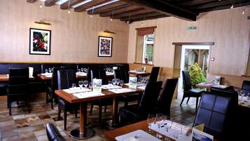 Un restaurant aux murs en bois, aux chaises en cuir noir et aux tables dressées pour le repas.