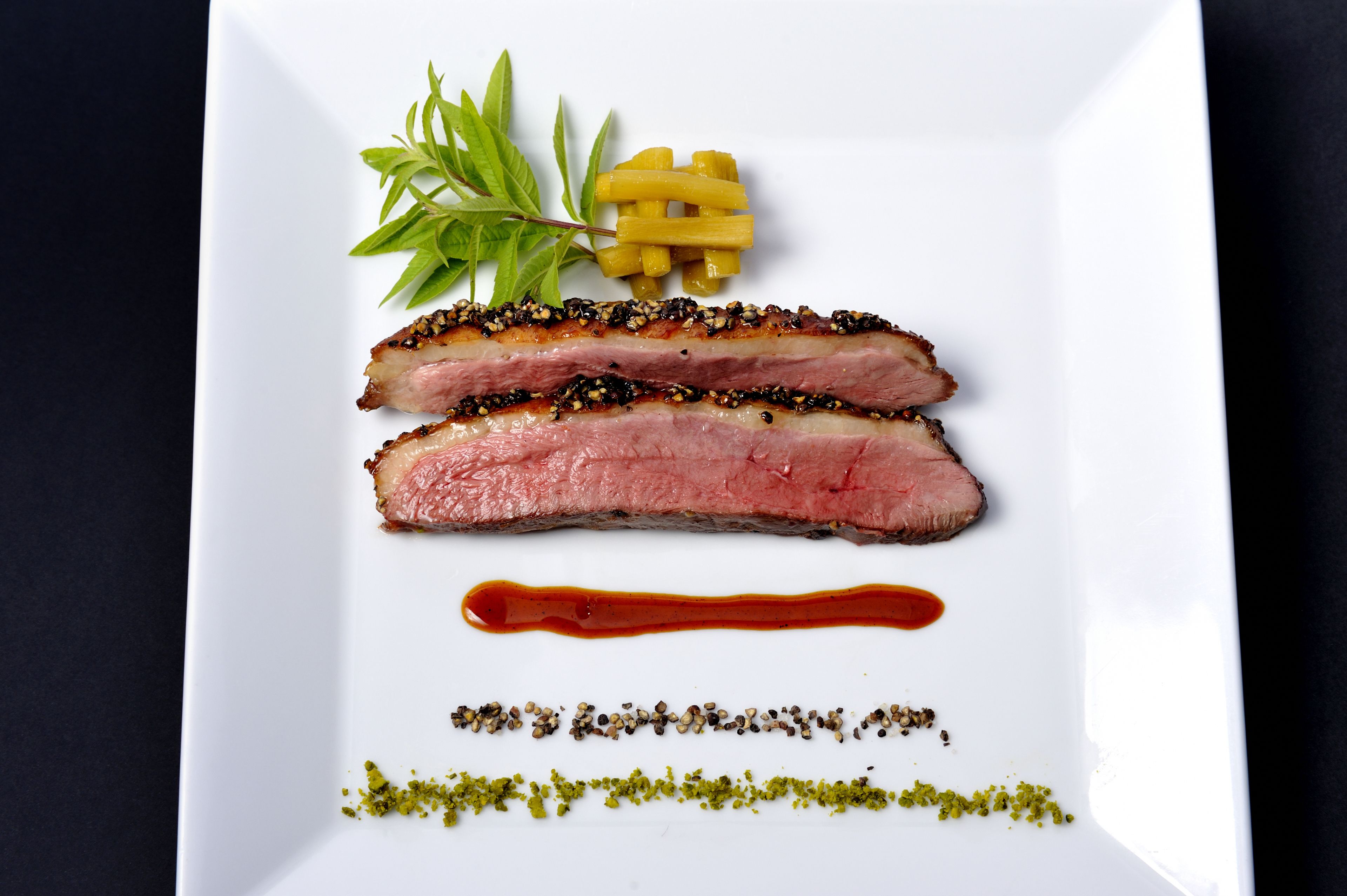 A white plate with two slices of meat, a small bunch of green leaves, and a few yellow items.