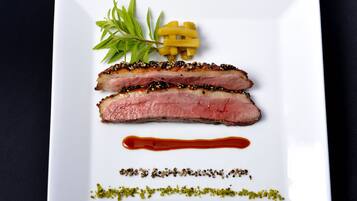 A white plate with two slices of meat, a small bunch of green leaves, and a few yellow items.