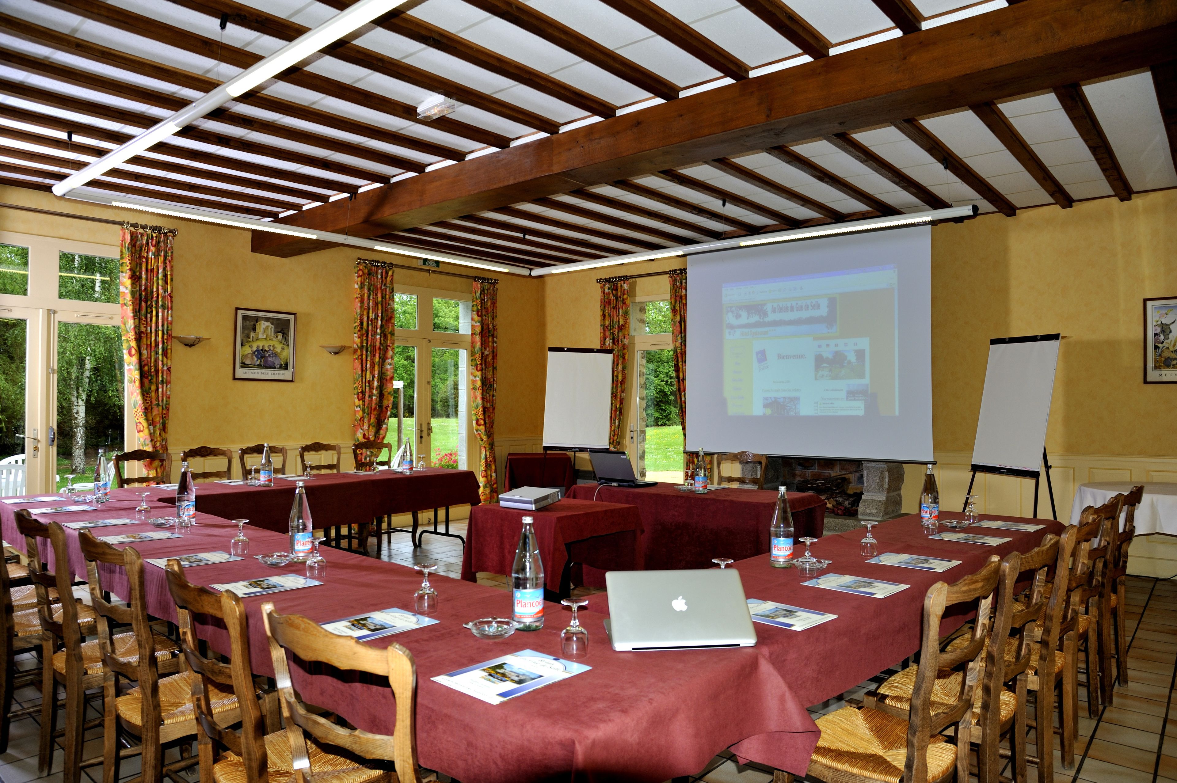 A conference room with long tables, wooden chairs, and a projector screen displaying a presentation.