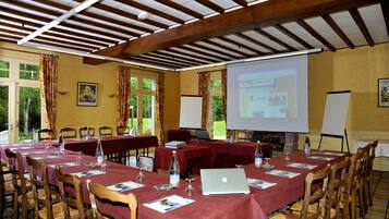 A conference room with long tables, wooden chairs, and a projector screen displaying a presentation.