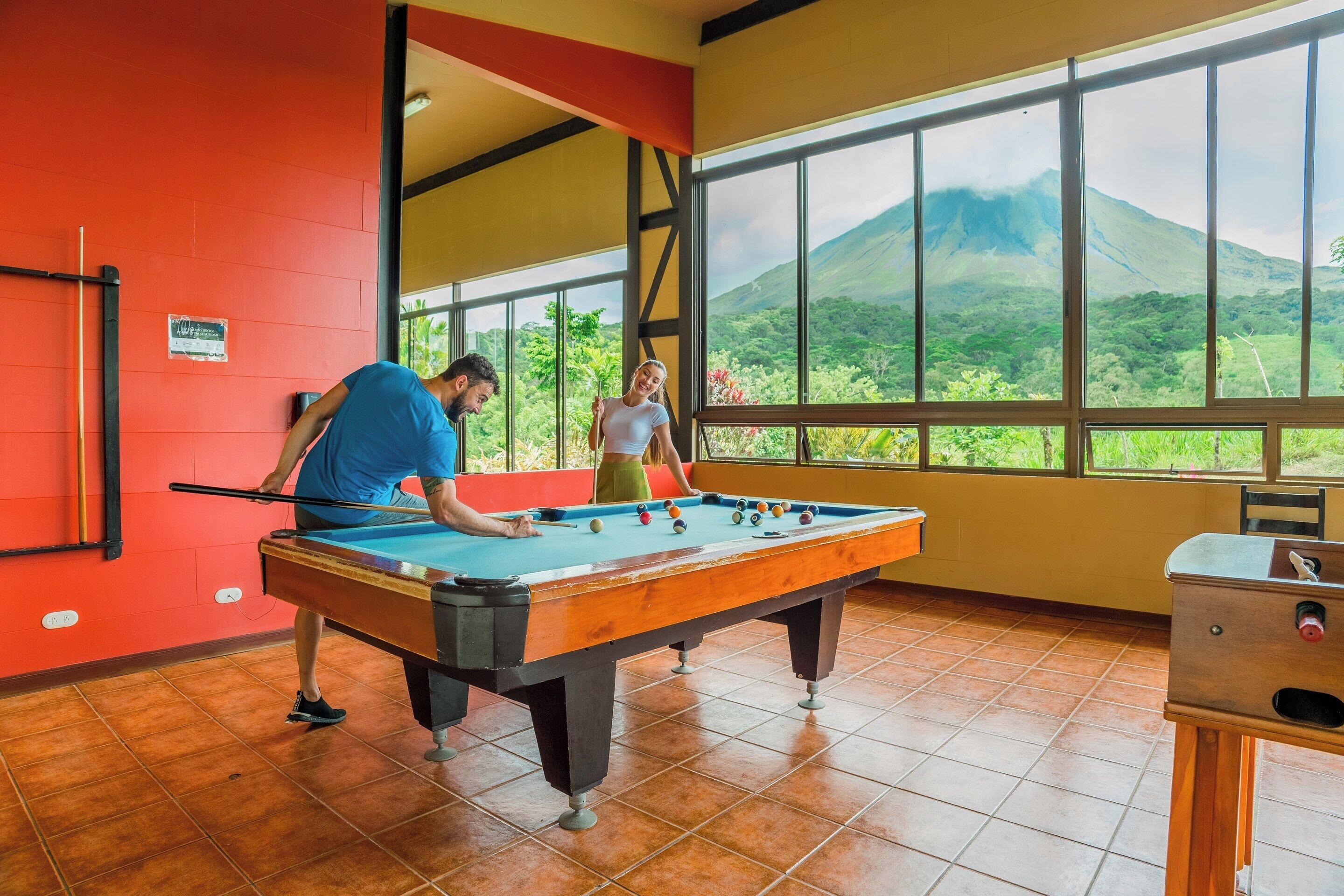A pool table in a room with large windows overlooking a mountain.