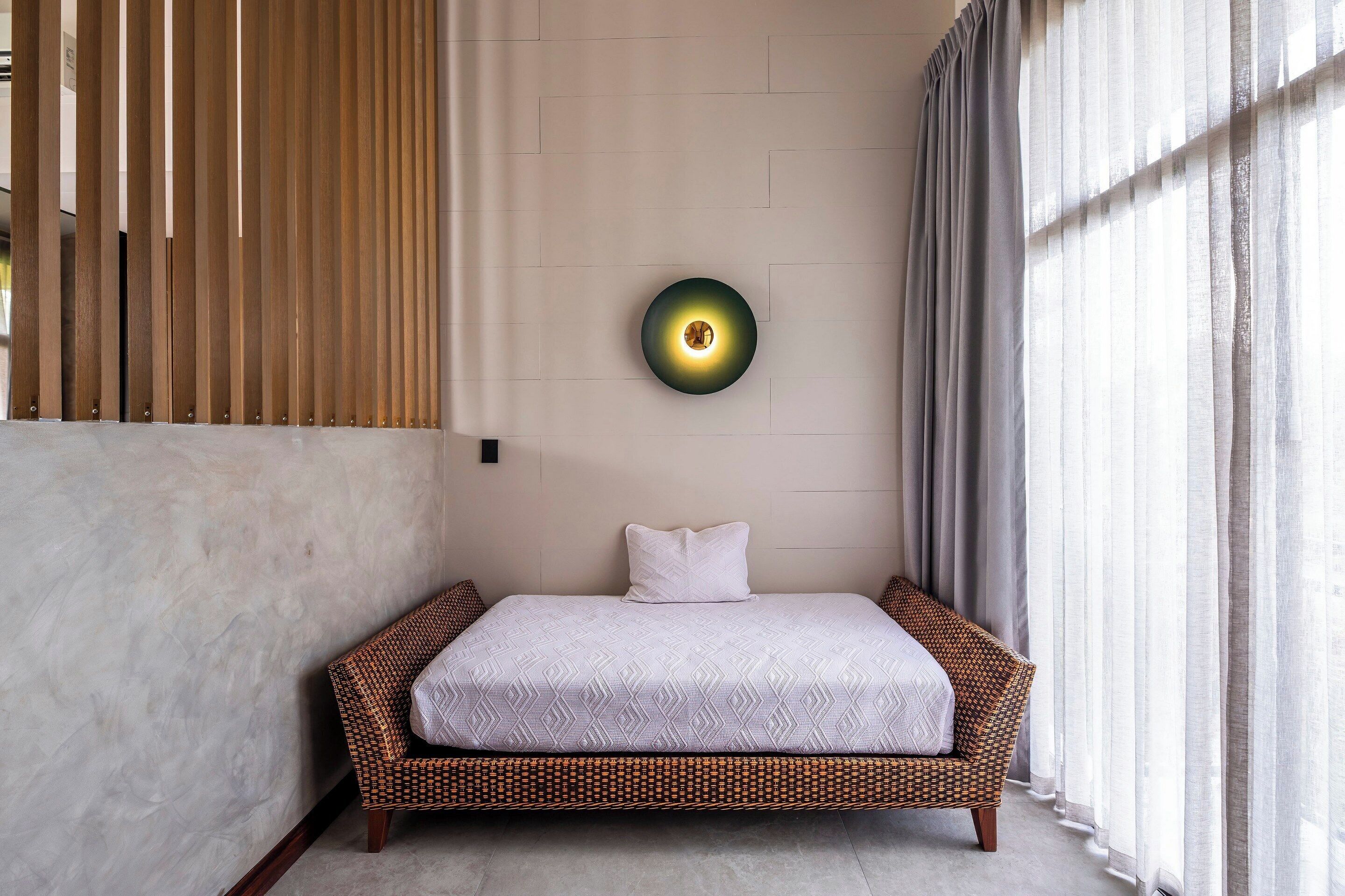 A room with a bed, a wall-mounted light, and a window with curtains.
