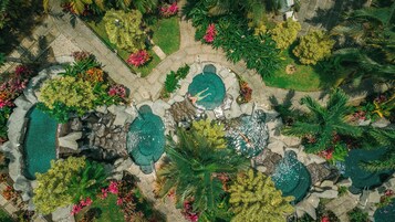 Vista aérea de una zona ajardinada con múltiples piscinas, rodeada de diversos tipos de vegetación y senderos de piedra.
