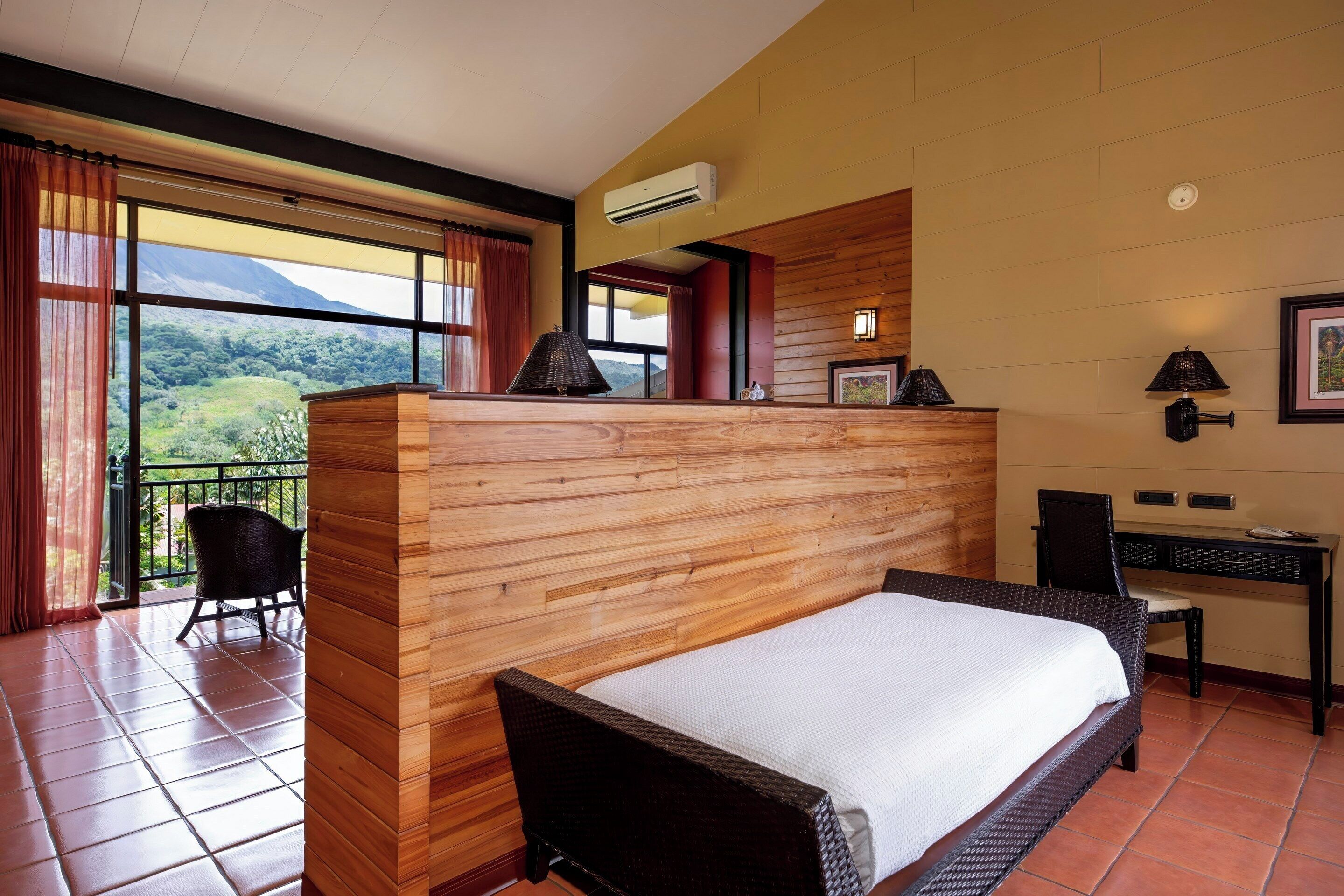 Habitación de hotel con cama, escritorio y silla. Tiene un balcón con vistas a las montañas.