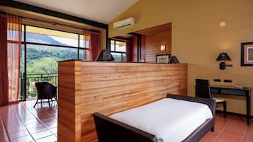 Habitación de hotel con cama, escritorio y silla. Tiene un balcón con vistas a las montañas.