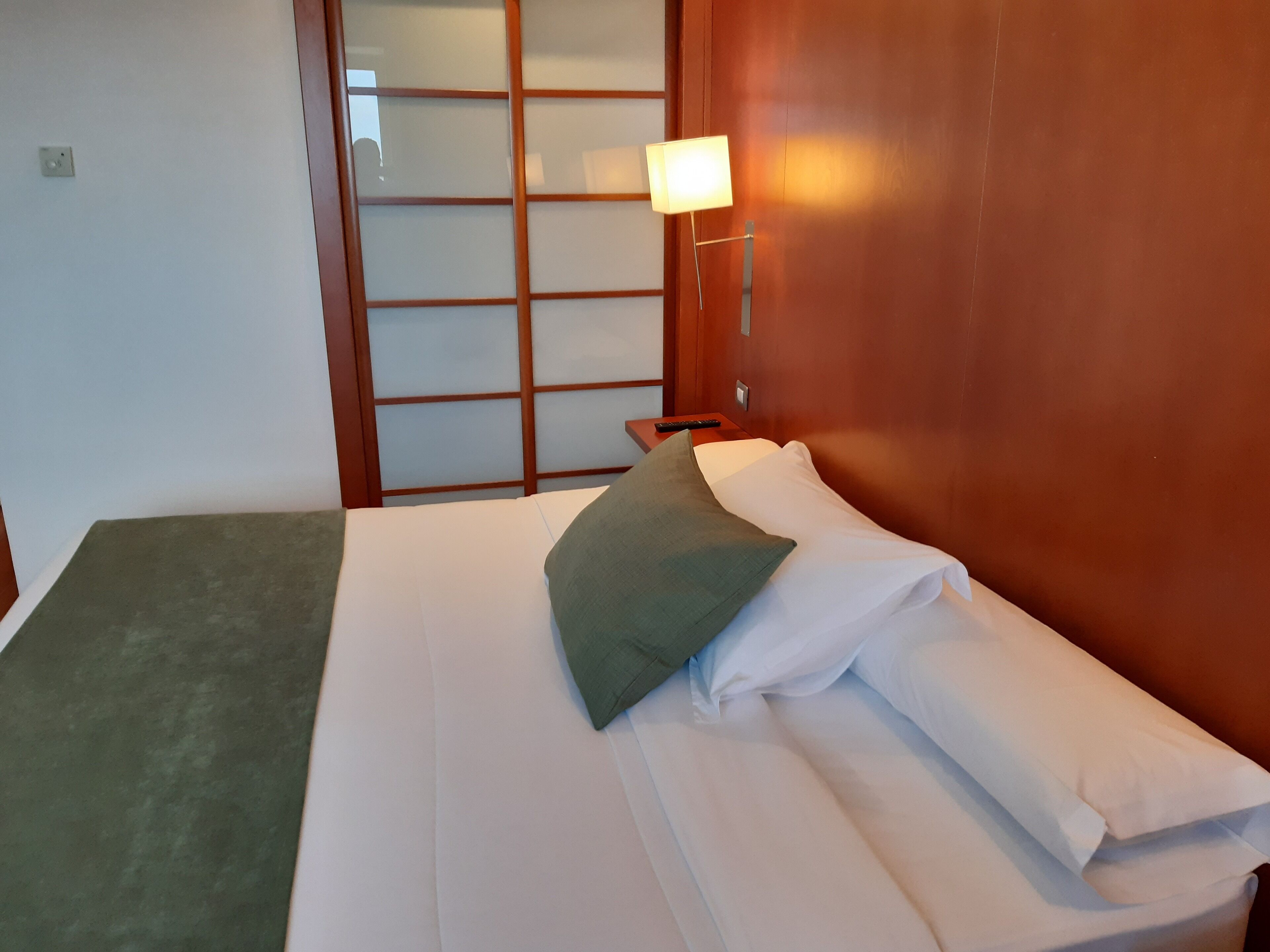 Una habitación de hotel con cama, mesita de noche, lámpara y puerta corredera.