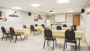 Ein Konferenzraum mit mehreren Tischen, Stühlen, einem Projektor und einer Tafel.