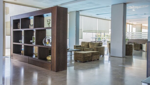 A modern lobby with a wooden bookshelf, comfortable seating, and large windows. - Hotel Xon's Valencia (Quart de Poblet)