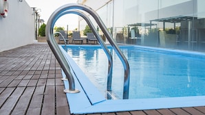 A swimming pool with a metal ladder, wooden deck, and a modern building with large windows in the background. - Hotel Xon's Valencia (Quart de Poblet)