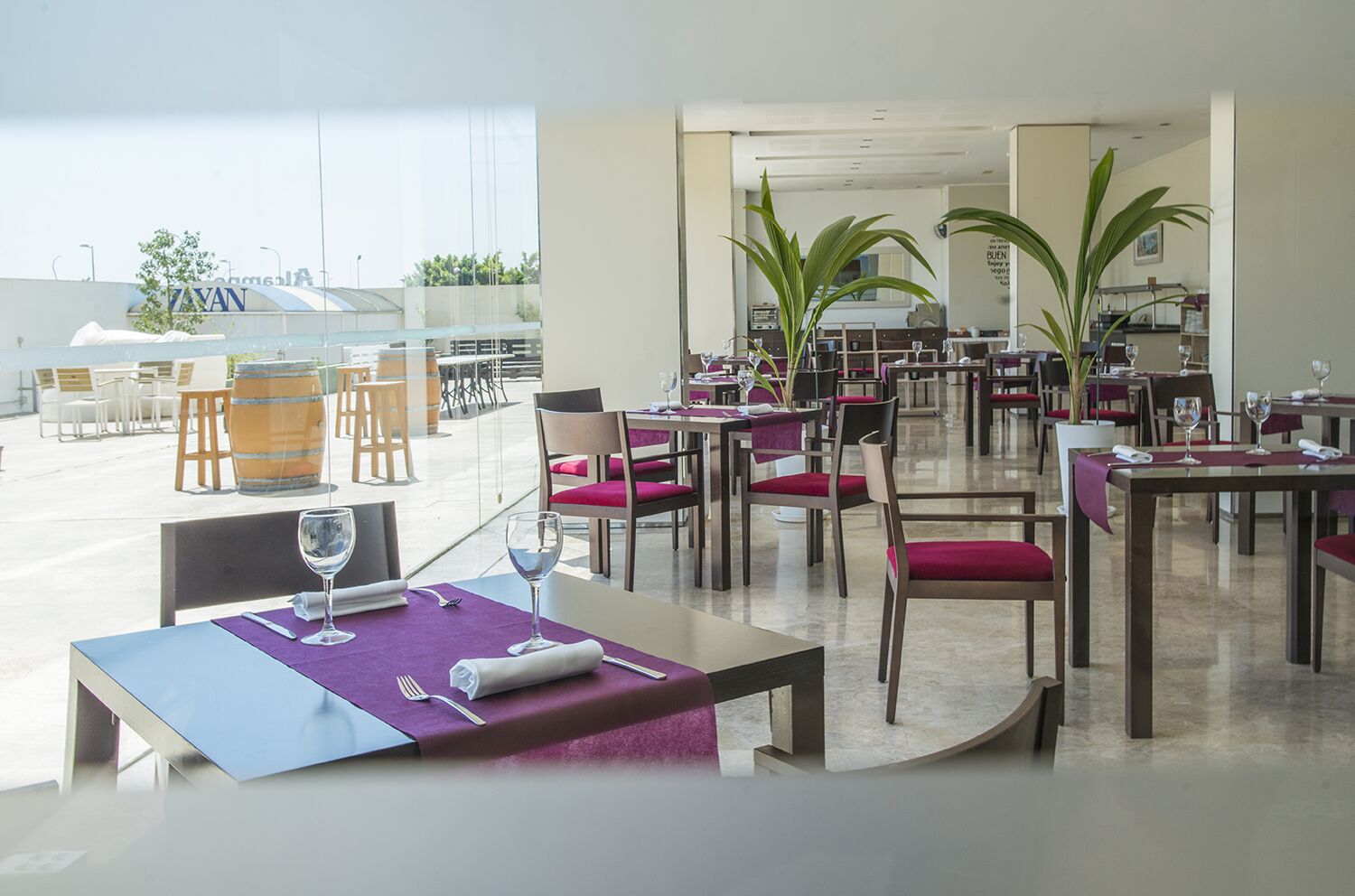 Een ruim restaurant met meerdere tafels en stoelen, grote ramen en potplanten.