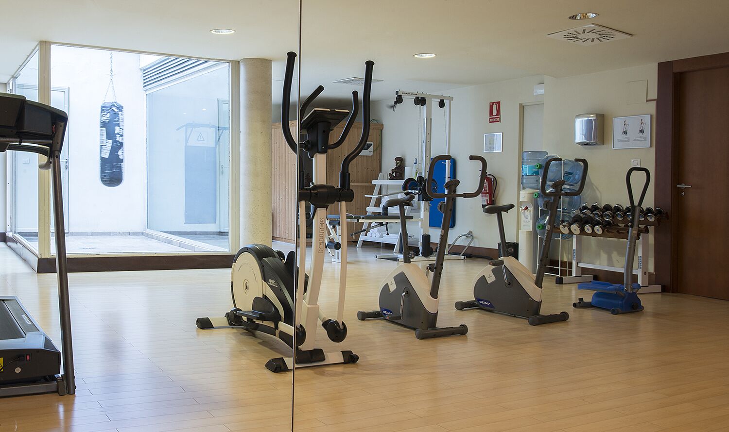 Une salle de sport équipée de divers appareils d’exercice, d’un sac de frappe et d’un distributeur d’eau.