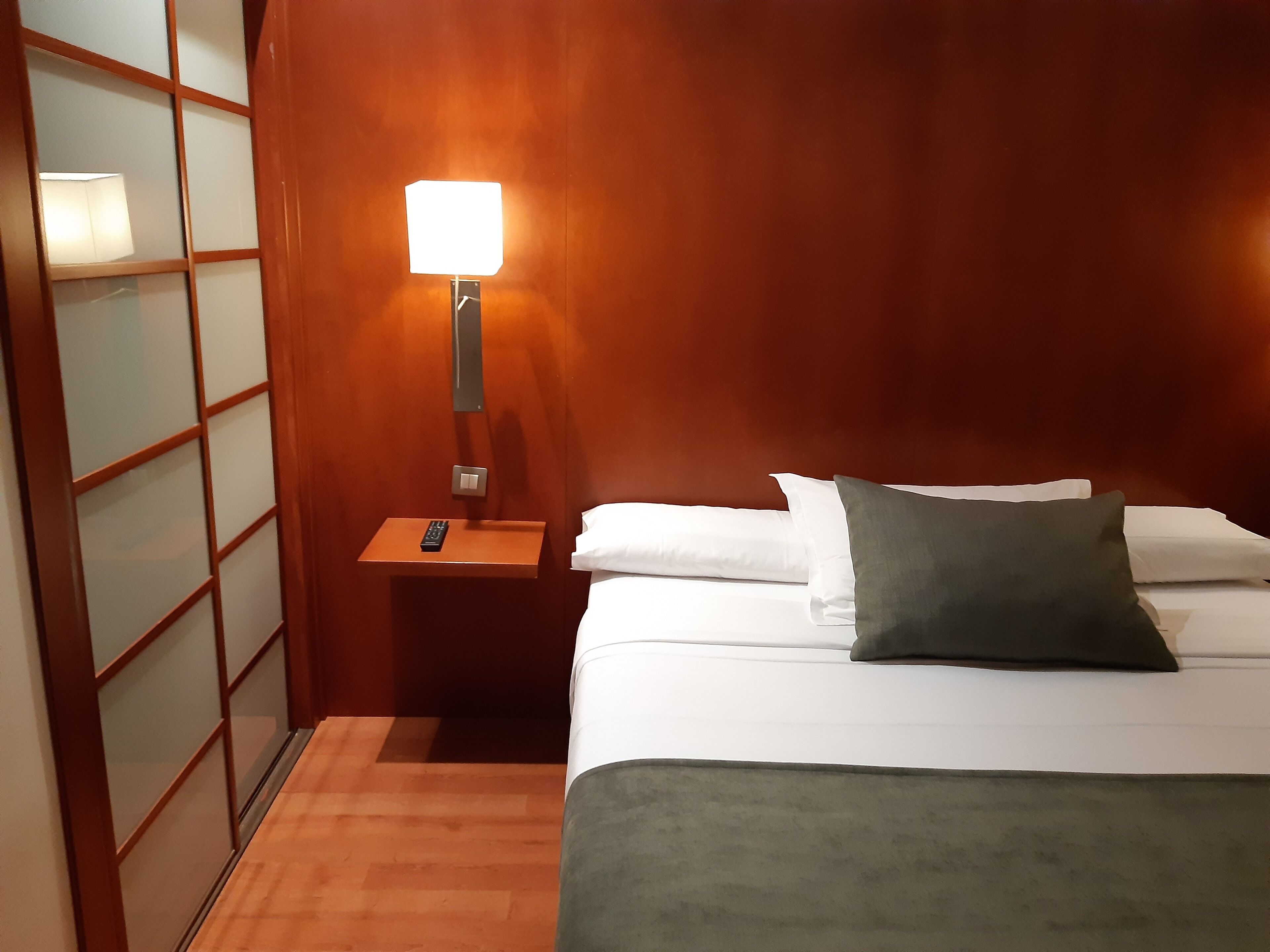 Ein Hotelzimmer mit einem Bett, einem Nachttisch mit Lampe und einer Wand aus Holzpaneelen.
