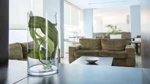A clear glass vase with a plant on a table in a modern, well-lit room with a sofa and a plant in the background. - Hotel Xon's Valencia (Quart de Poblet)