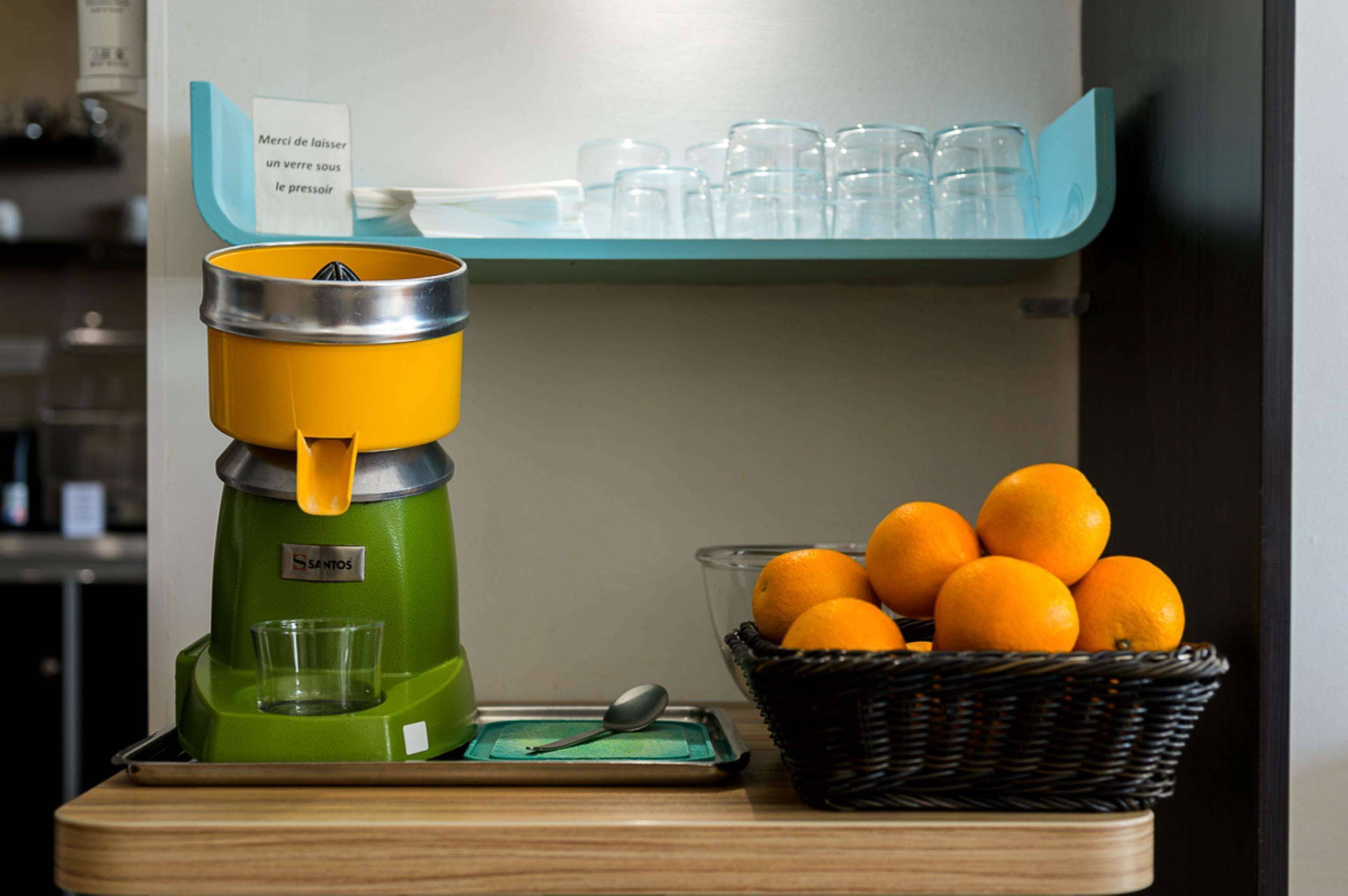 A beverage dispenser with a basket of oranges and a tray with a spoon.