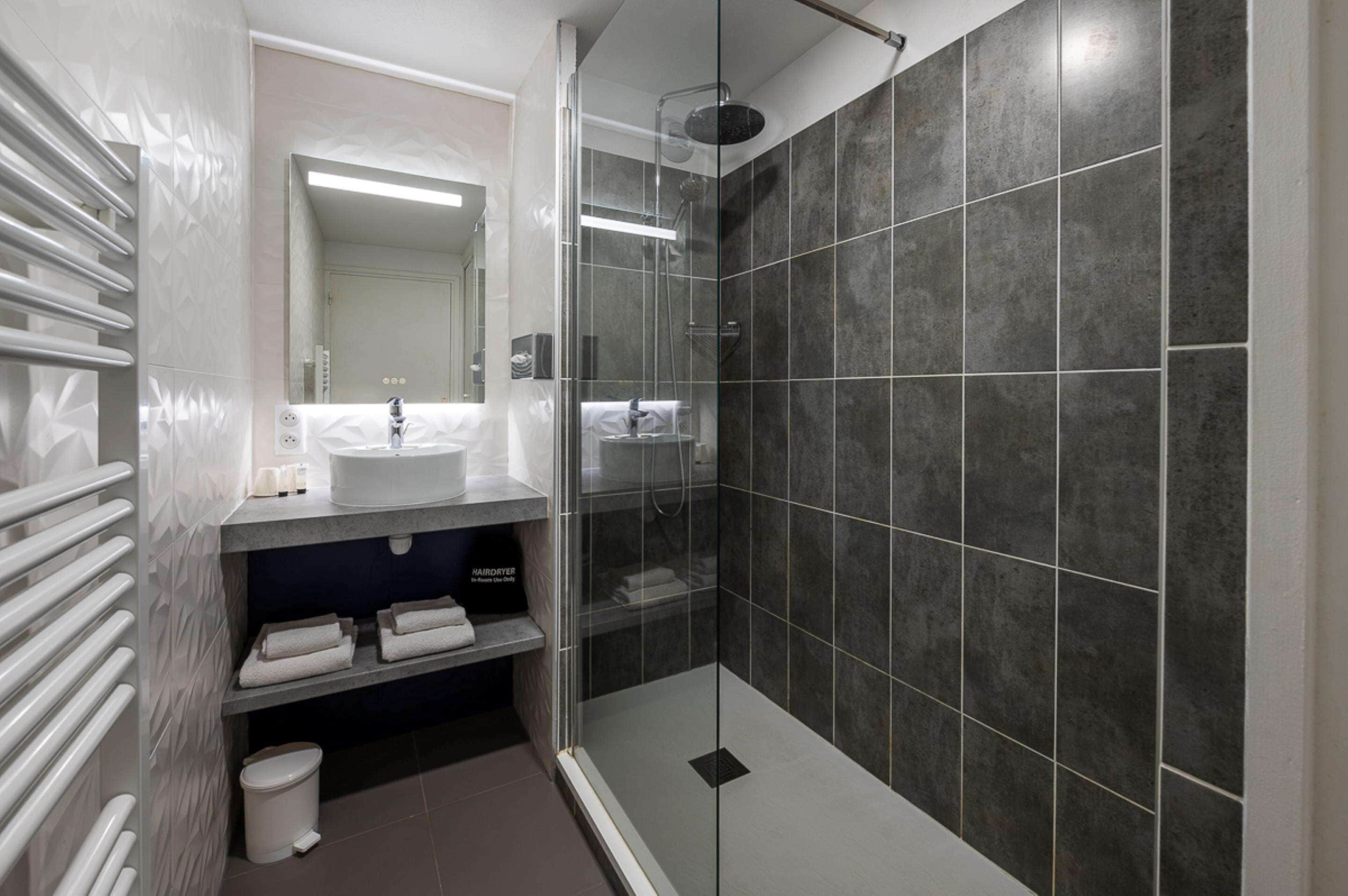 A modern bathroom with a glass-enclosed shower, a vanity with a sink, and a towel rack.
