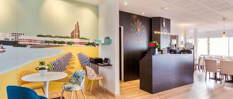 Un moderno vestíbulo de hotel con un mural, un mostrador de recepción, zona de estar y un espacio para comer.