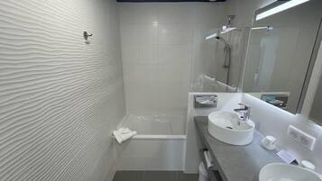 A modern bathroom with a textured wall, a bathtub, a large mirror, and two sinks.