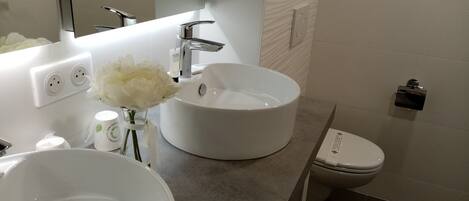 A modern bathroom with a white sink, a mirror, and a toilet.