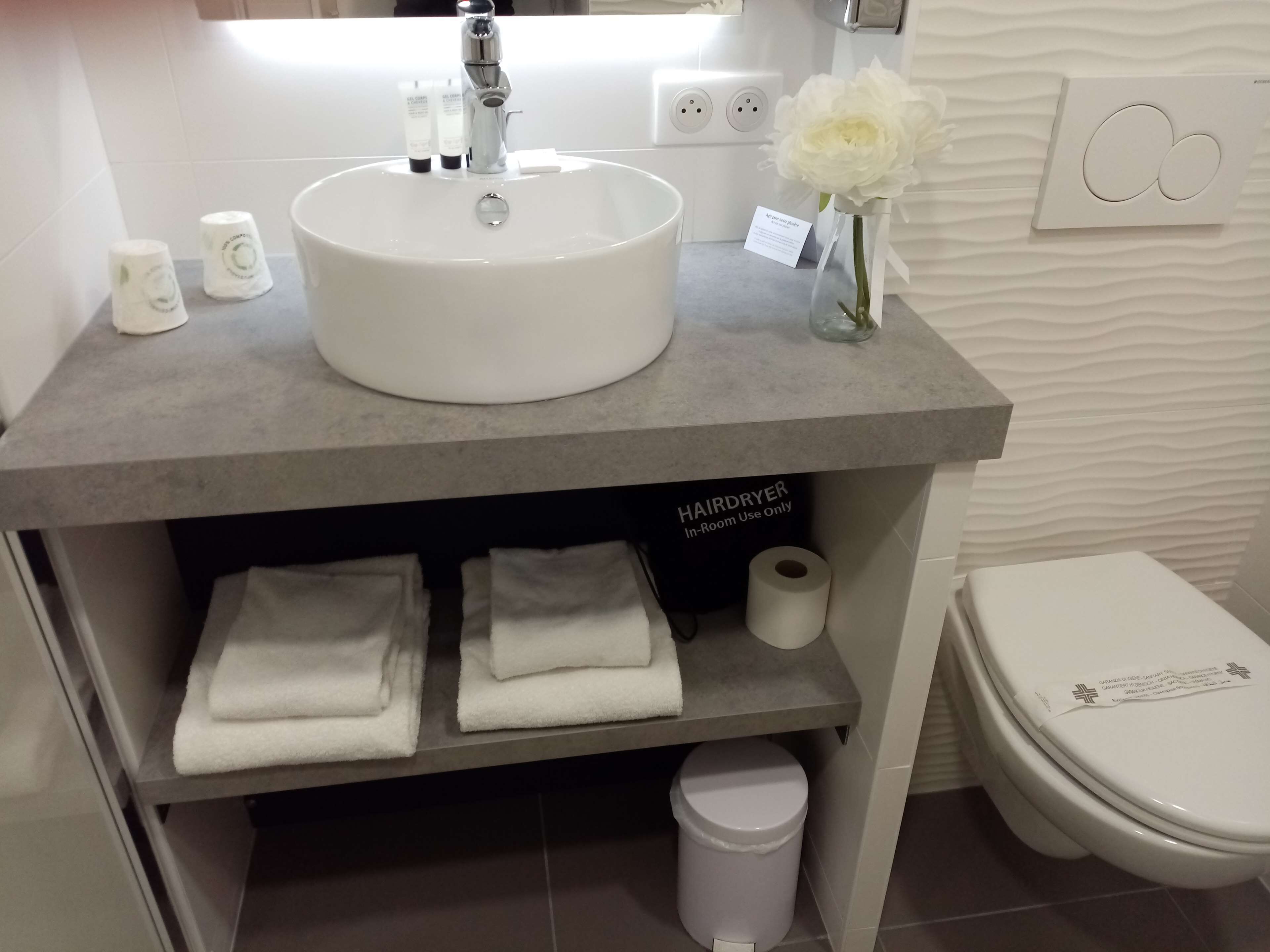 Un bagno con un lavandino bianco, un asciugacapelli e asciugamani piegati con cura.