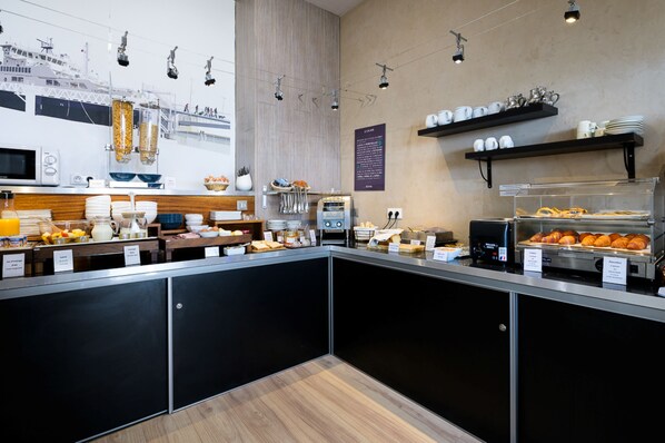 Una barra de desayuno moderna con diversas opciones de comida, una máquina de café y una vitrina con pasteles.