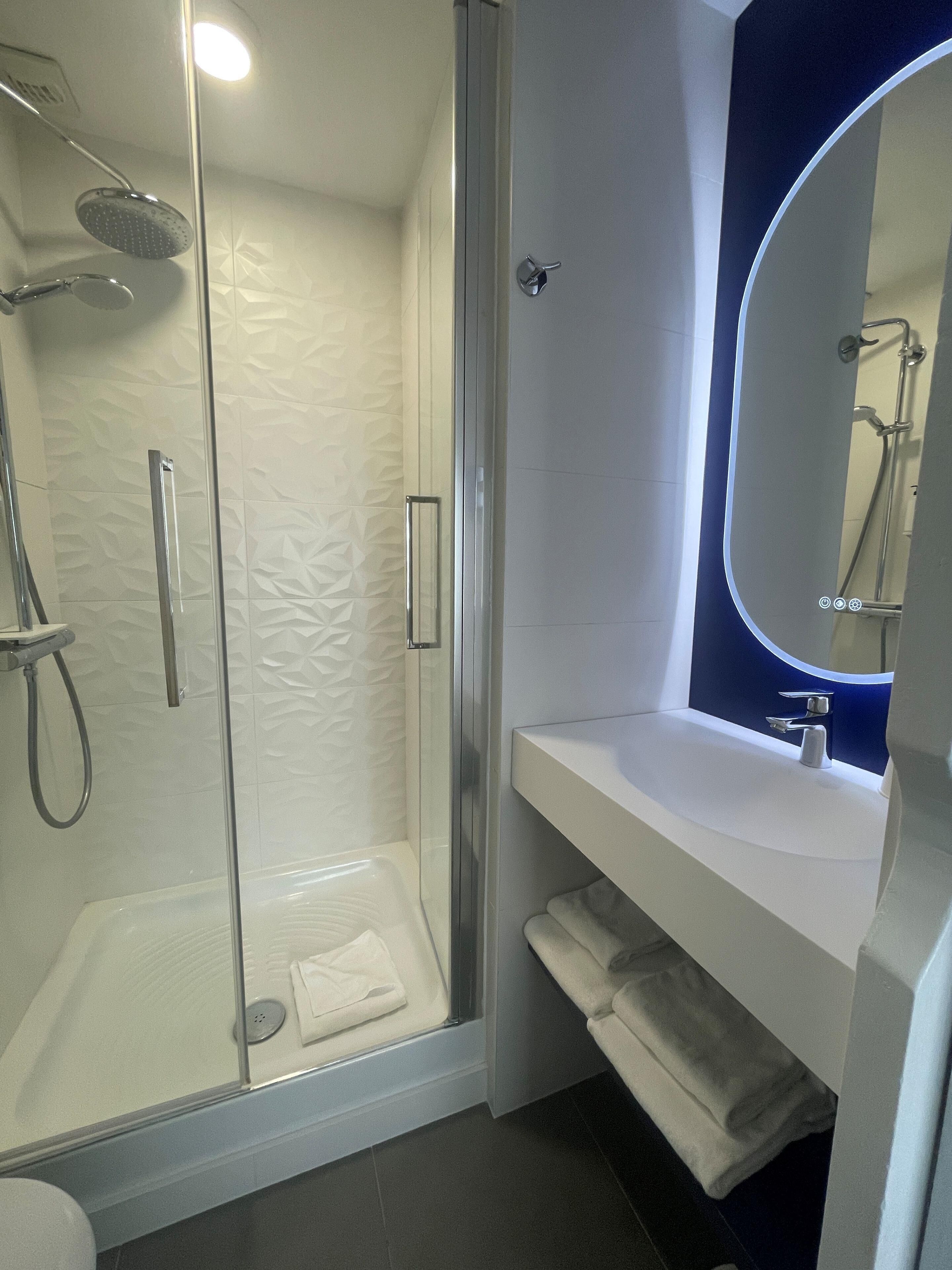 Un baño moderno con ducha de vidrio, un lavabo blanco con espejo y un perchero para toallas.