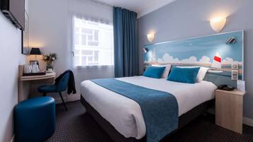 A hotel room with a bed, a desk, a chair, a nightstand, and a wall with a decorative light fixture.