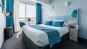 A modern hotel room with a large bed, a view of the city, a small desk, and a chair.