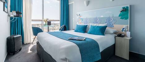 A modern hotel room with a large bed, a view of the city, a small desk, and a chair.