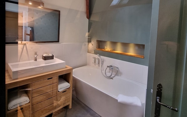 A modern bathroom with a large bathtub, a vanity with a mirror, and a shelf above the bathtub. - Manoir d'Hautegente (Coly-Saint-Amand)