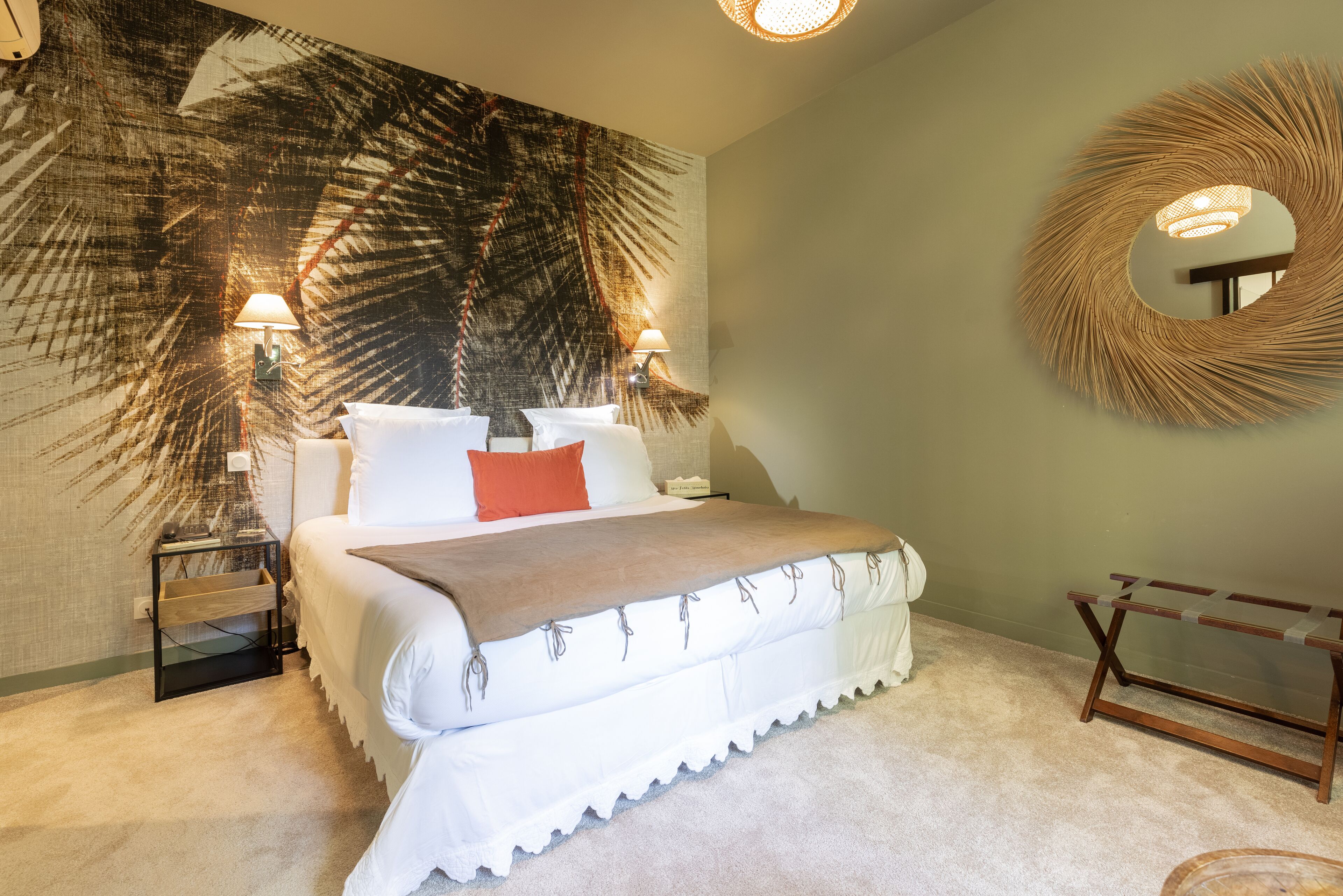 A bedroom with a large bed, two bedside lamps, a round mirror, and a wall tapestry.