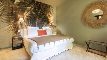 A bedroom with a large bed, two bedside lamps, a round mirror, and a wall tapestry.