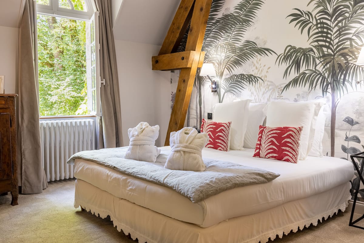 Un dormitorio con una cama grande, una escalera de madera, una ventana con cortinas y un mural de palmeras.