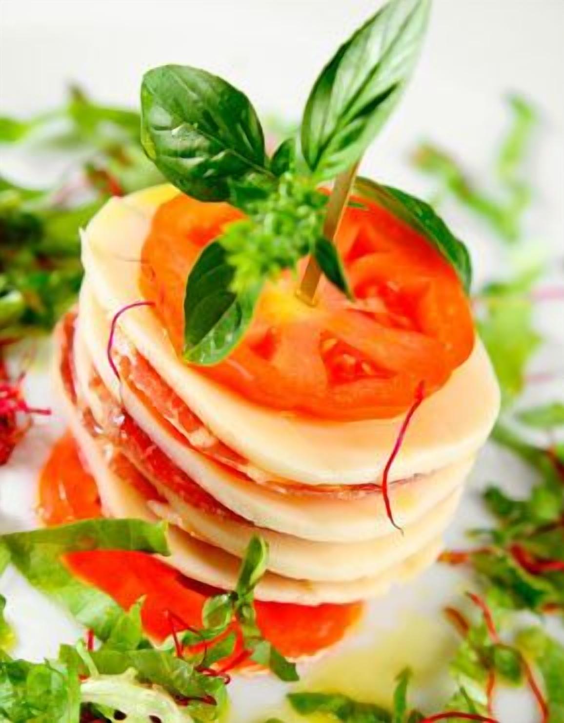 A layered dish with tomatoes, basil, and a toothpick.