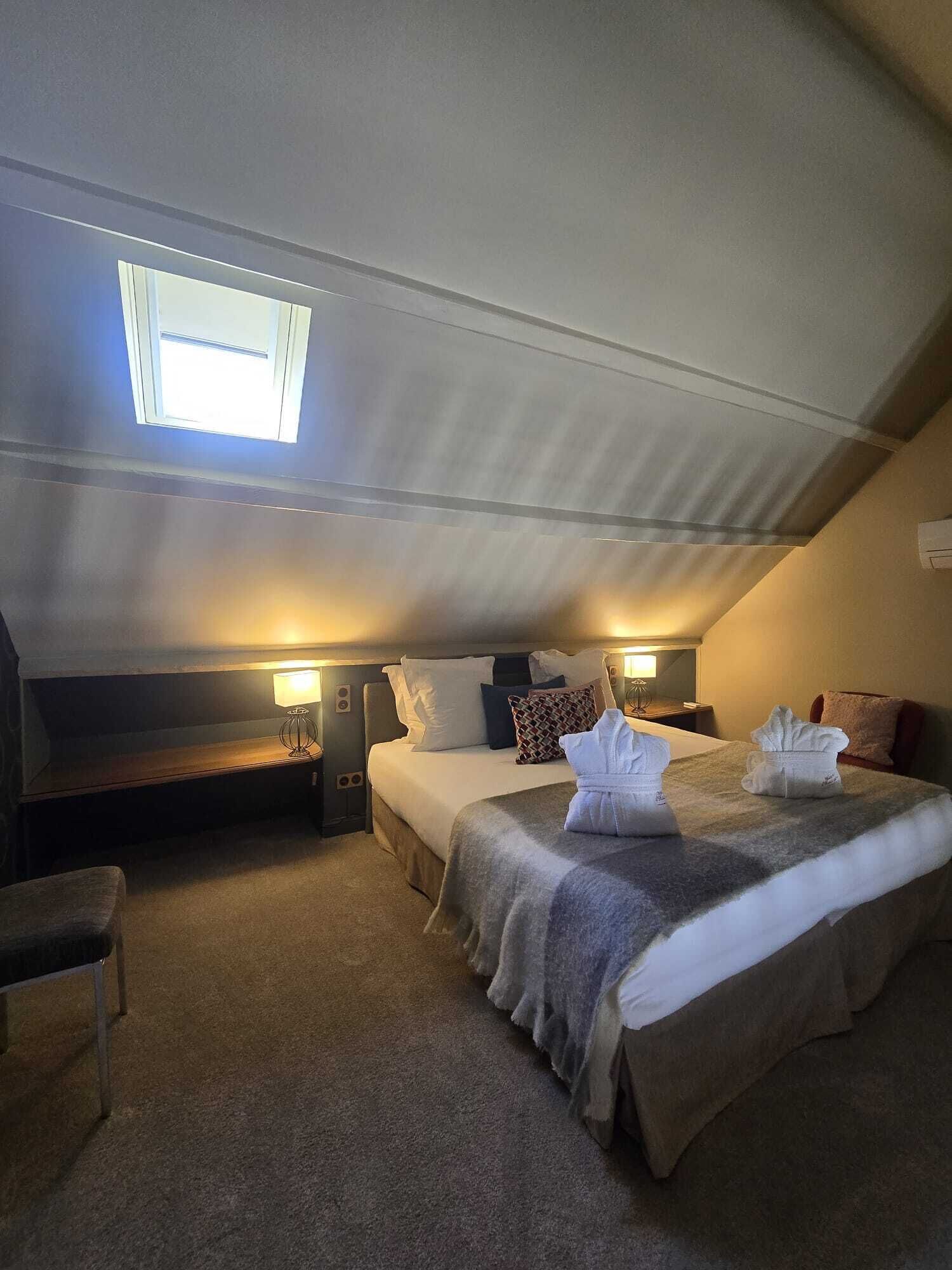 Une pièce chaleureuse et faiblement éclairée, avec un grand lit, deux tables de chevet et une petite fenêtre.