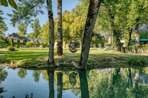 A serene lakeside setting with a hammock hanging between trees, a house with ivy-covered walls, and a clear reflection in the water. - Manoir d'Hautegente (Coly-Saint-Amand)