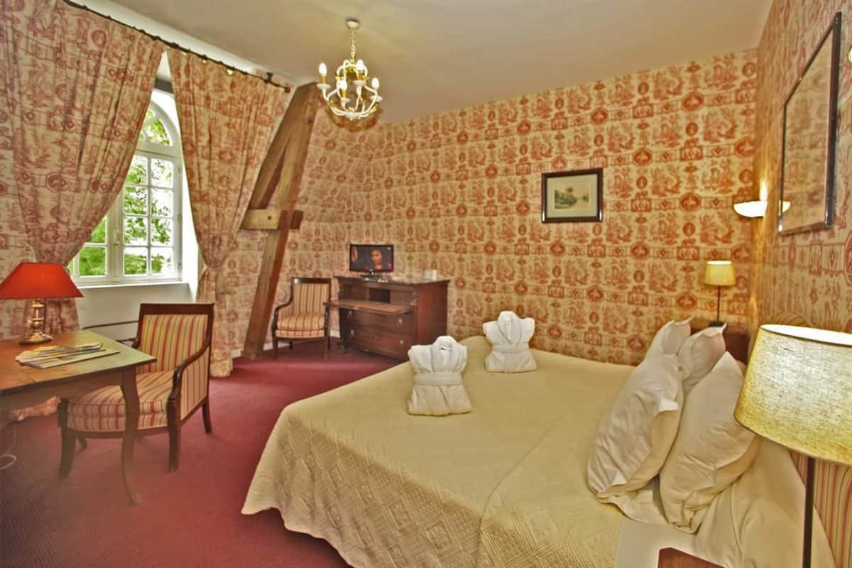 Habitación de hotel con una cama grande, un escritorio, una silla, un televisor y un ventanal con cortinas.