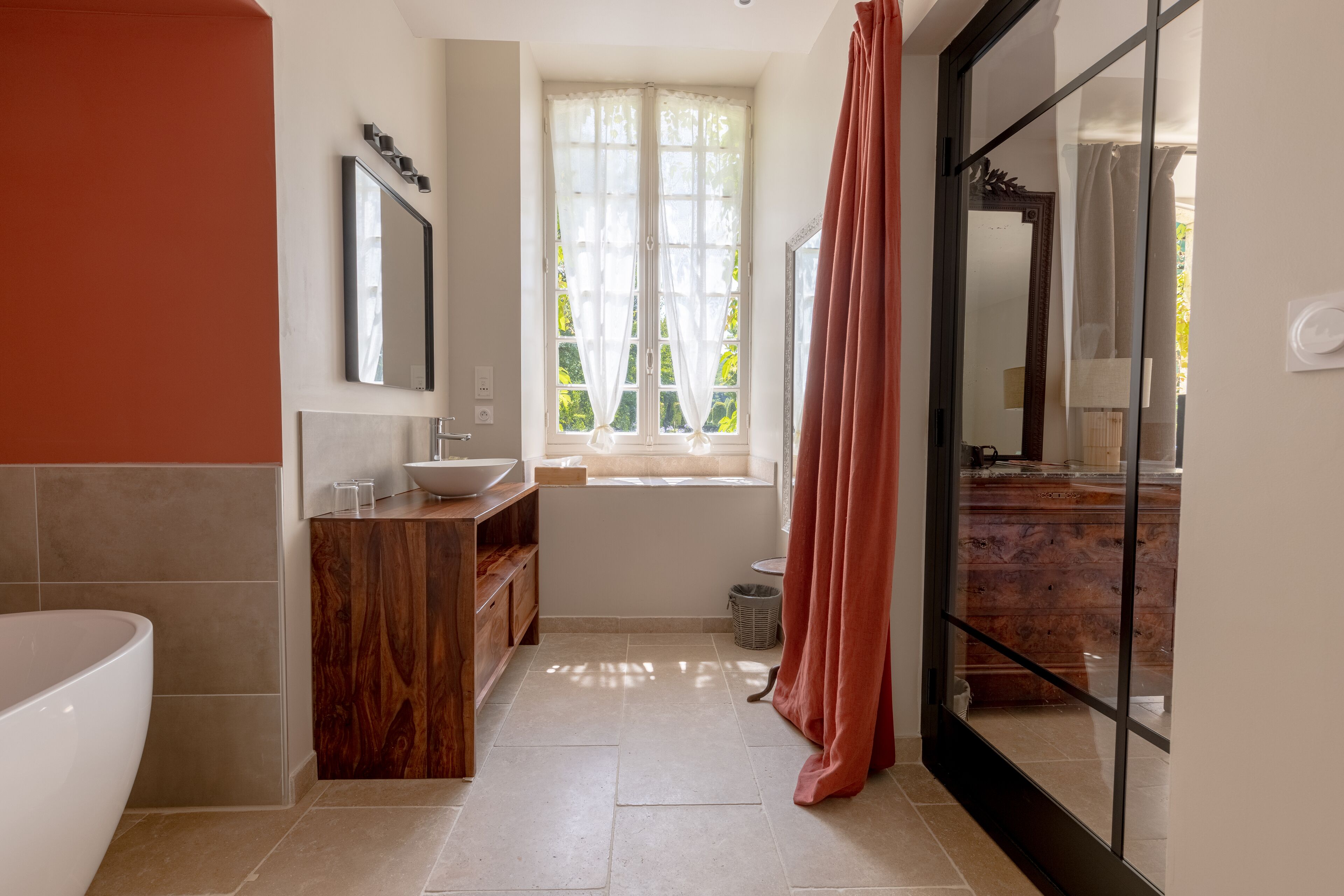 A bathroom with a bathtub, vanity, and window with curtains.
