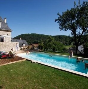 A swimming pool area with a stone house, a grassy lawn, and a view of the surrounding hills. - Manoir d'Hautegente (Coly-Saint-Amand)