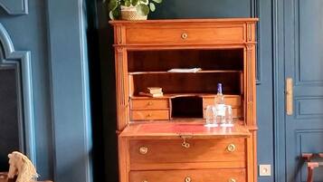 Une commode en bois avec des tiroirs et une étagère, une petite plante posée sur le dessus et une bouteille en verre sur l’étagère.