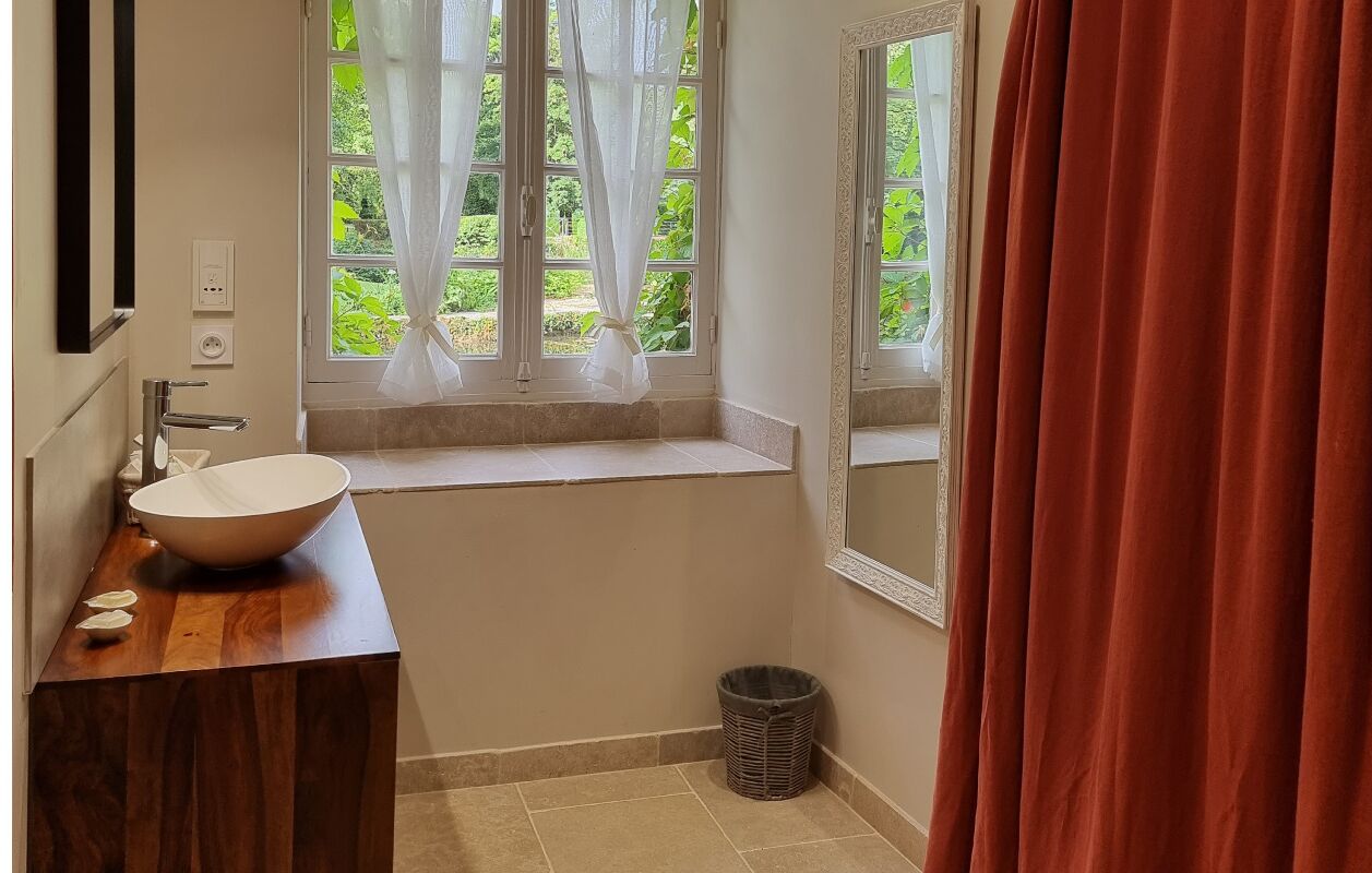 A bathroom with a wooden vanity, a white sink, a window with sheer curtains, and a red curtain.