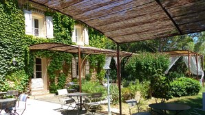 An outdoor patio with tables and chairs, a covered seating area, and a stone building with ivy. - La Sommellerie (Chateauneuf-du-Pape)