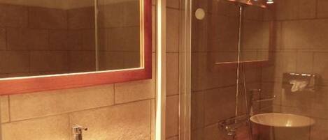 A bathroom with a wooden vanity, a large mirror, a round sink, and a shower area.