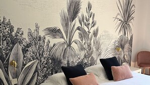 A bedroom with a bed, two pillows, a bedside table, and a wall with a botanical print. - La Sommellerie (Chateauneuf-du-Pape)