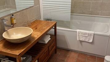 A bathroom with a wooden vanity, a large sink, a mirror, a bathtub, and a shower.