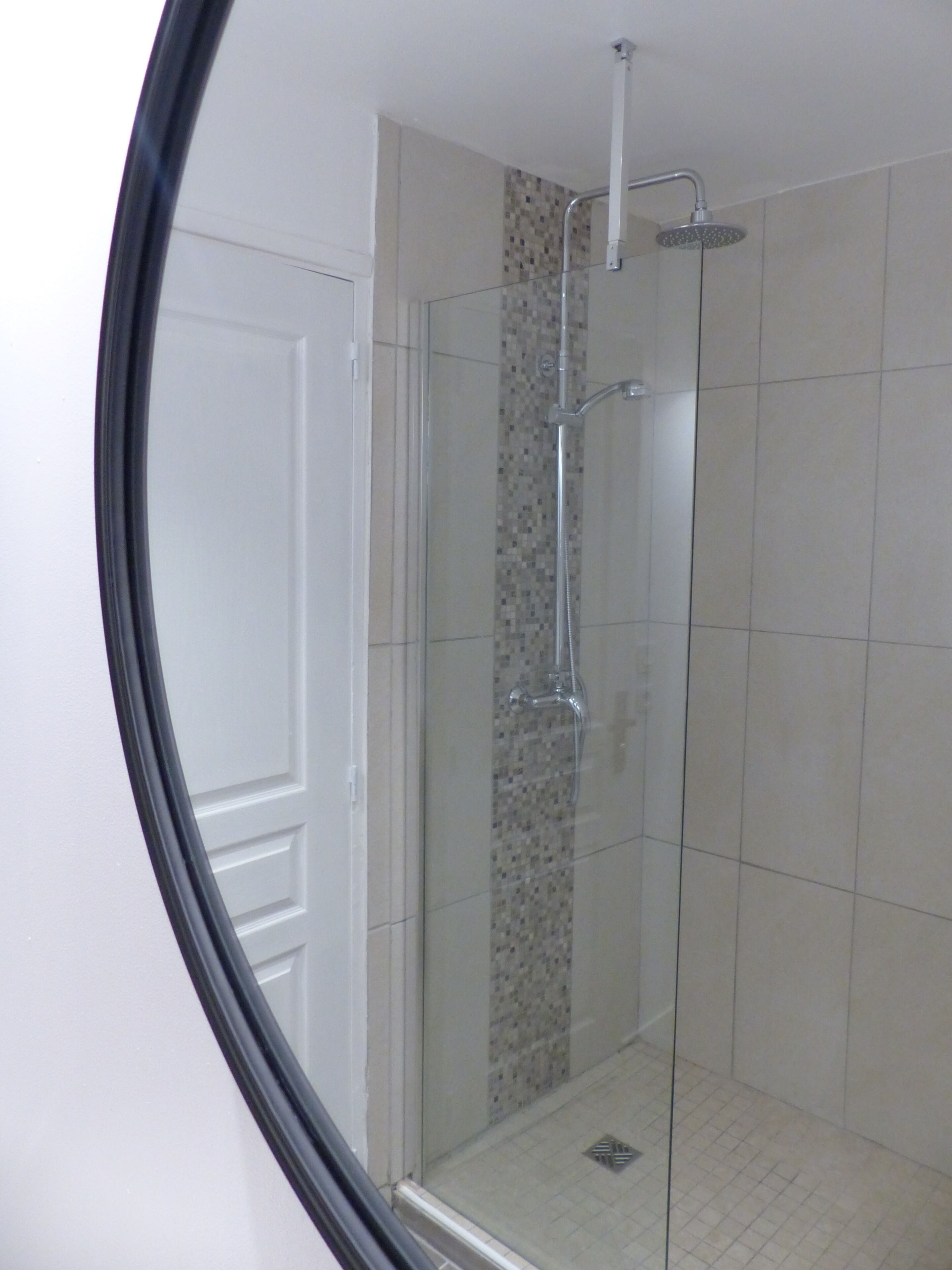 Une douche entièrementClose avec des parois en verre, un sol carrelé et un mur décoratif orné de mosaïques.