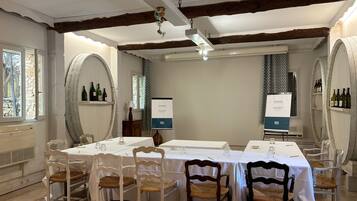 A dining area with white tables and chairs, wooden beams on the ceiling, and wine bottles on shelves.